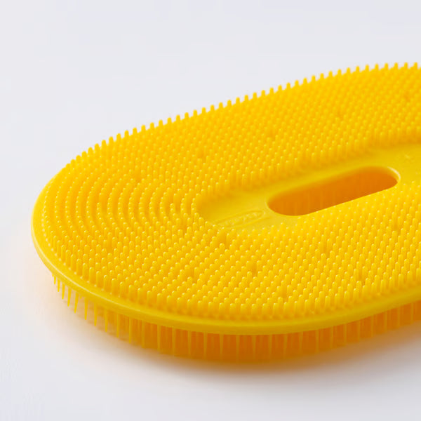 Person using IKEA UPPFYLLD yellow vegetable scrubber to clean potatoes on kitchen counter showing dual scrubbing sides