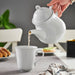 Minimalist IKEA UPPLAGA teapot in glossy white ceramic, holding 1.2 liters (1.3 quarts) of tea, with drip-free spout and heat-resistant design.
