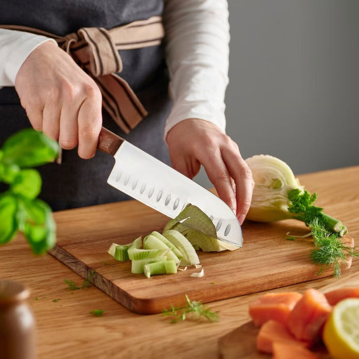 Person slicing vegetables on a wooden cutting board with a knife