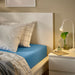 Bed styled with IKEA VÅRVIAL blue fitted sheet, white pillows and bedside table setup