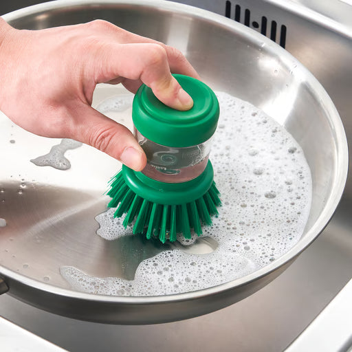 Person using IKEA VIDEVECKMAL green dish brush with dispenser to scrub a kitchen sink