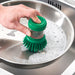 Person using IKEA VIDEVECKMAL green dish brush with dispenser to scrub a kitchen sink