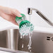Person holding IKEA VIDEVECKMAL green dish brush under tap to rinse while dispensing soap