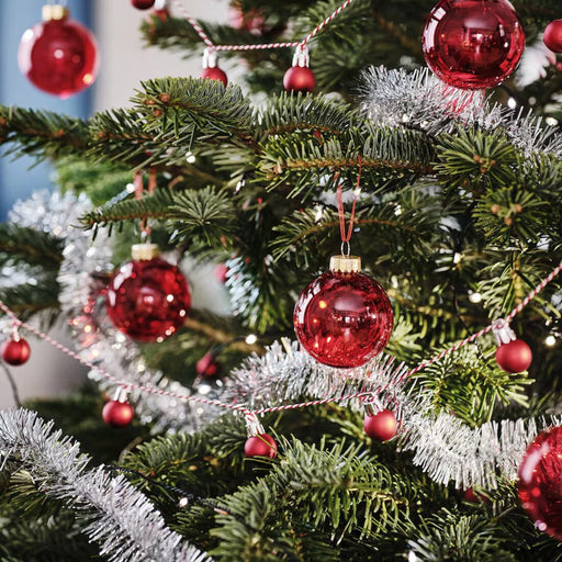 IKEA VINTERFINT red glass bauble hanging on a Christmas tree branch, sparkling under holiday lights.