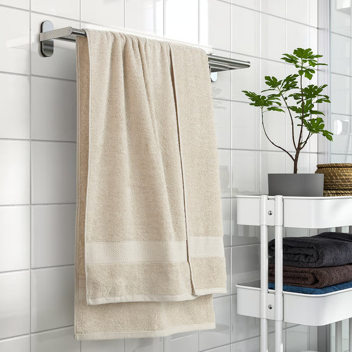 IKEA VITBACKEN beige bath towel hanging on a rail with a hanging loop, near tiles and shelves of folded towels