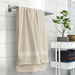 IKEA VITBACKEN beige bath towel hanging on a rail with a hanging loop, near tiles and shelves of folded towels