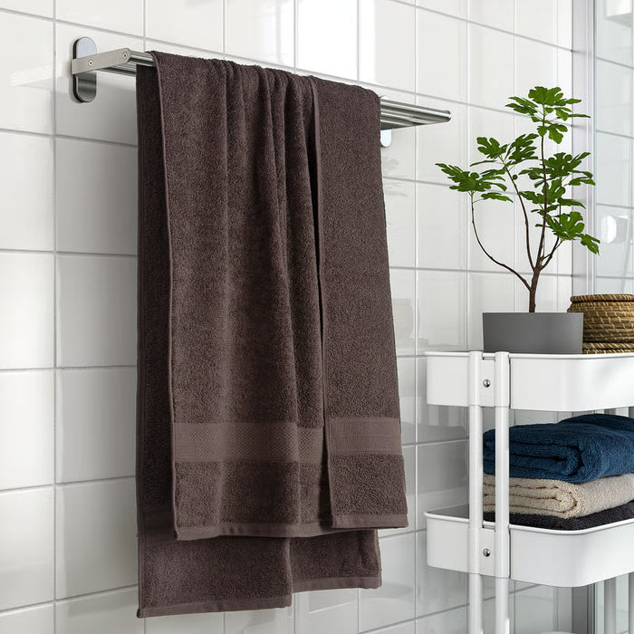 IKEA VITBACKEN brown cotton bath towel hanging on a rack beside folded towels and a potted plant on a white shelf