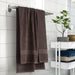IKEA VITBACKEN brown cotton bath towel hanging on a rack beside folded towels and a potted plant on a white shelf