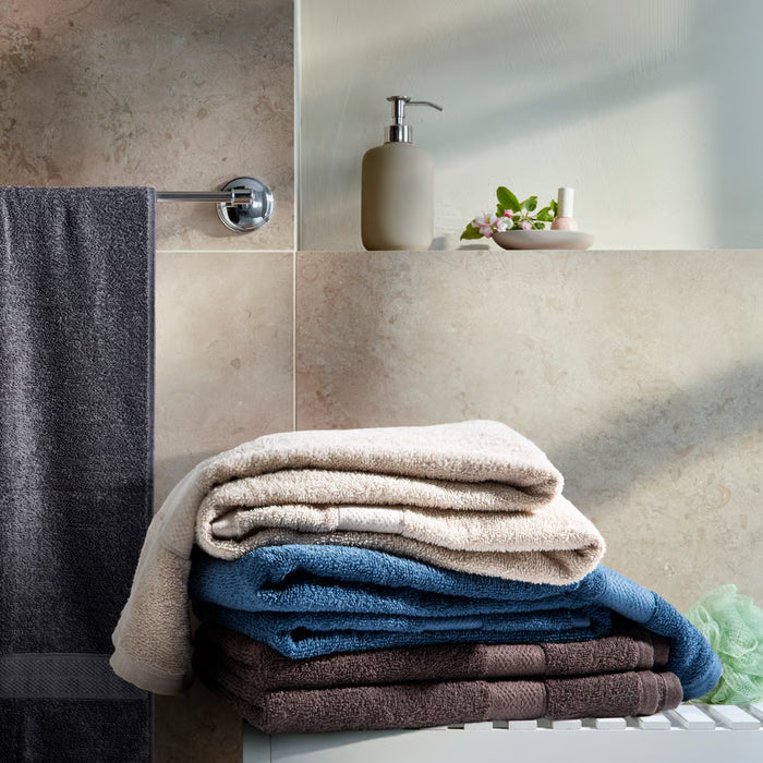 IKEA VITBACKEN brown bath towel stacked with white and blue towels in a bathroom with beige tiled wall