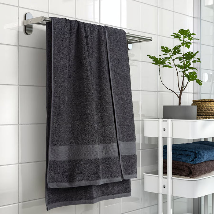 IKEA VITBACKEN dark grey bath towel hanging on a silver rail, larger than folded towels on a white shelf with a plant