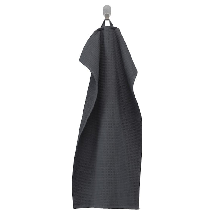 An anthracite hand towel from the Ikea 6 Piece Combo Set, hanging from a towel hook on a beige bathroom wall.