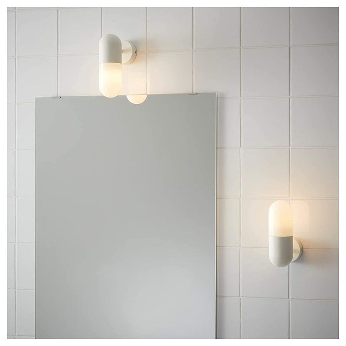 An LED IKEA Wall Lamp illuminating a cozy bathroom, with a book and a pair of glasses on a nightstand ‎80314271