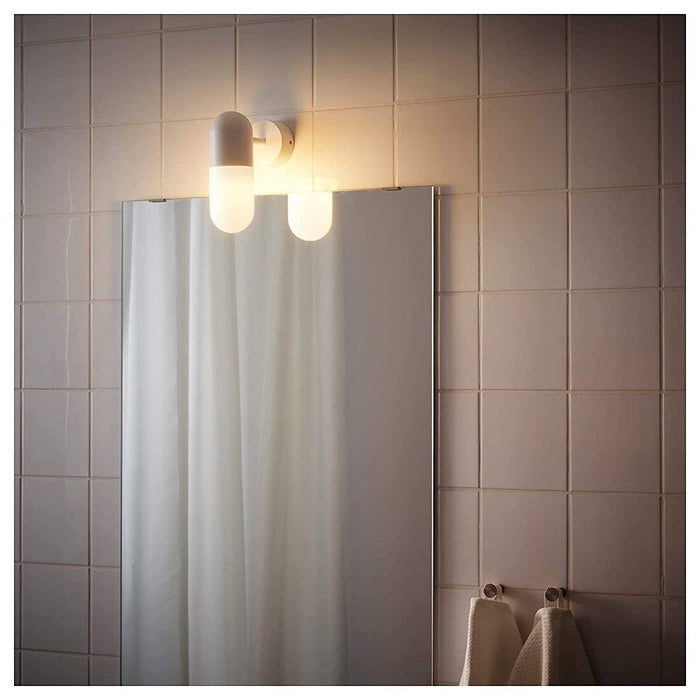 An LED IKEA Wall Lamp illuminating a cozy bathroom, with a book and a pair of glasses on a nightstand ‎80314271