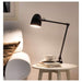 A black IKEA lamp with a flexible arm and a rounded shade, mounted on a white wall-40326025