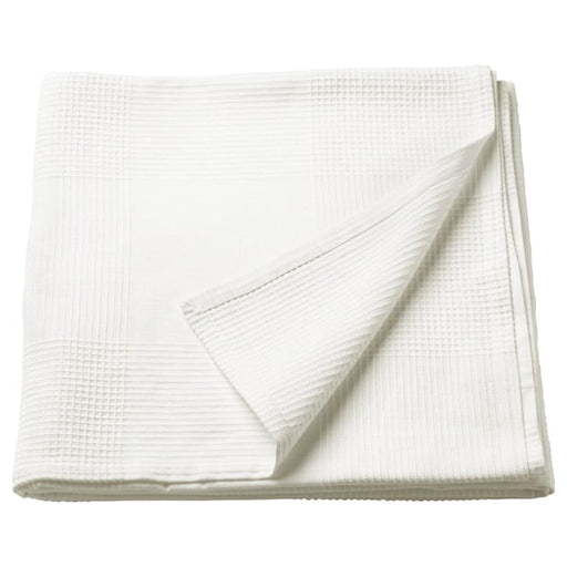 A white IKEA INDIRA Bedspread draped over a bed, with tassels hanging off the edges.