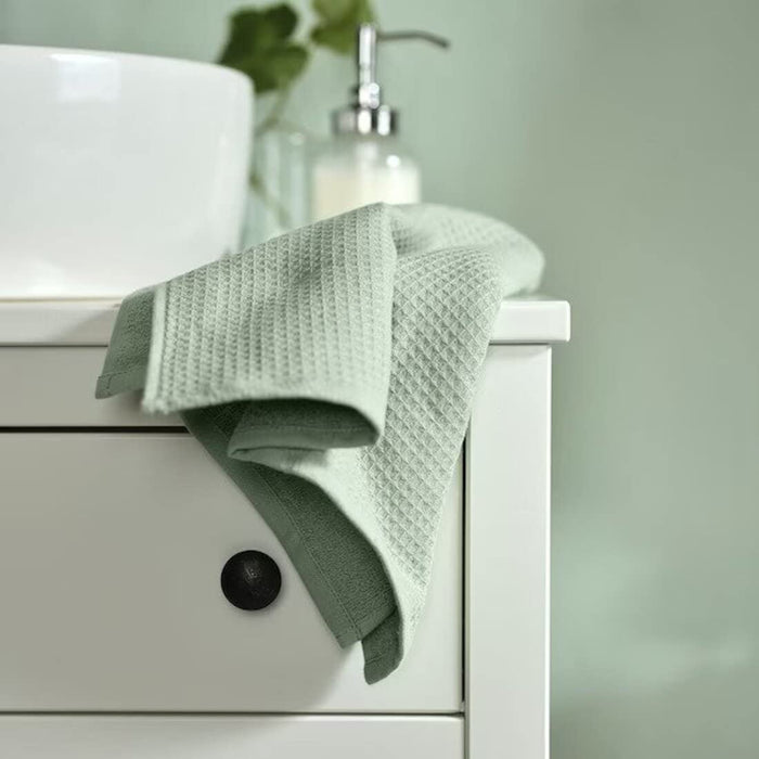A folded light green bath towel from the Ikea 6 Piece Combo Set, sitting on a wooden bathroom stool.