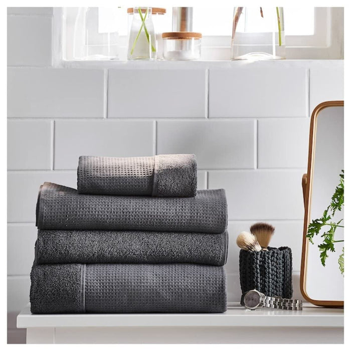 A folded anthracite bath towel from the Ikea 6 Piece Combo Set, sitting on a wooden bathroom stool.
