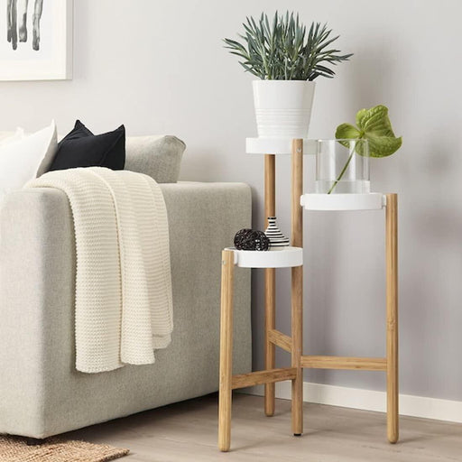 IKEA SATSUMAS white bamboo plant stand with green potted plants on multi-level shelves beside grey sofa