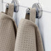 A dark beige hand towel from the Ikea 6 Piece Combo Set, hanging from a towel hook on a beige bathroom wall.