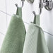A stack of four light green washcloths from the Ikea 6 Piece Combo Set, sitting on a white bathroom counter.