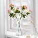 A lifelike artificial flower arrangement in a clear glass vase on a wooden tabletop.