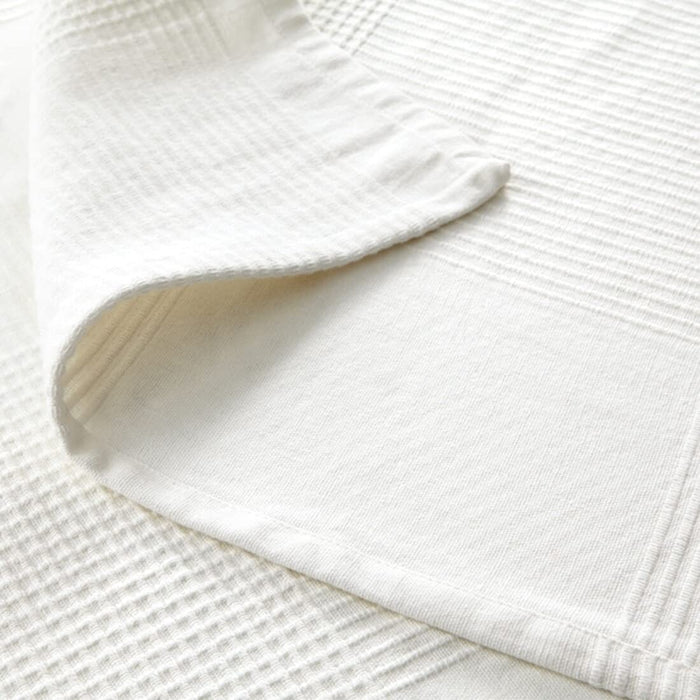 The white IKEA INDIRA Bedspread spread out on the ground, displaying its lightweight and airy quality.