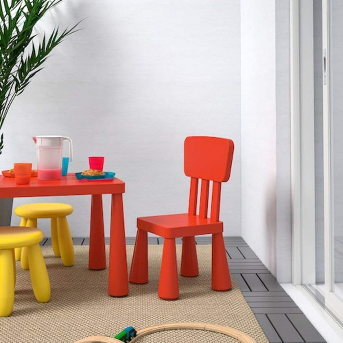 "A red IKEA Children's Chair on a grassy lawn, with a child playing with toys"