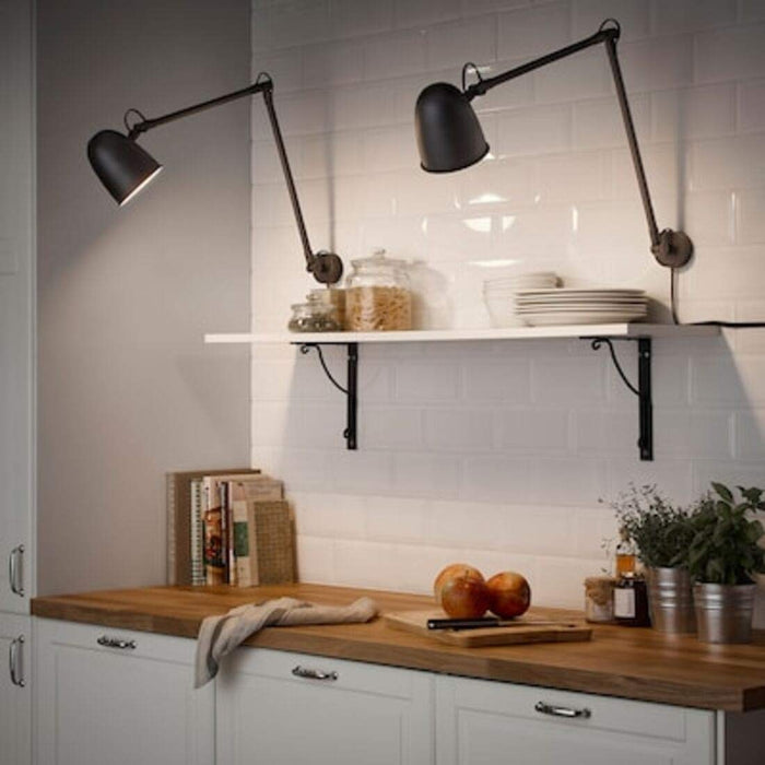 A black IKEA work lamp with a cone-shaped shade and a pivot arm, fixed to a white wall.-40326025