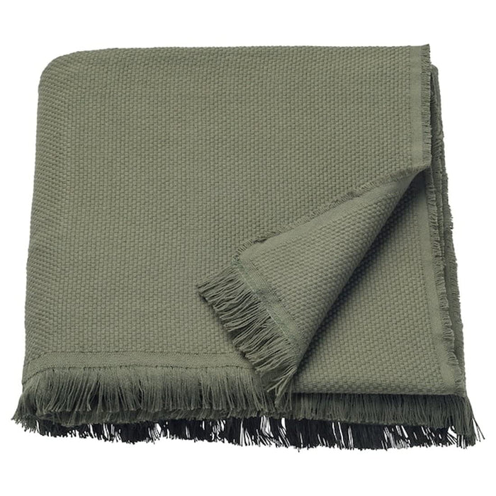 A cozy knit throw with tassels on each end, draped over a beige sofa.