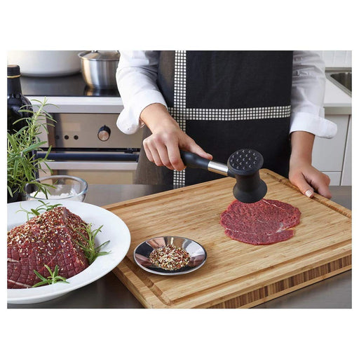 The black meat hammer being used to tenderize a piece of steak, with small dents visible on the surface of the meat  80163408