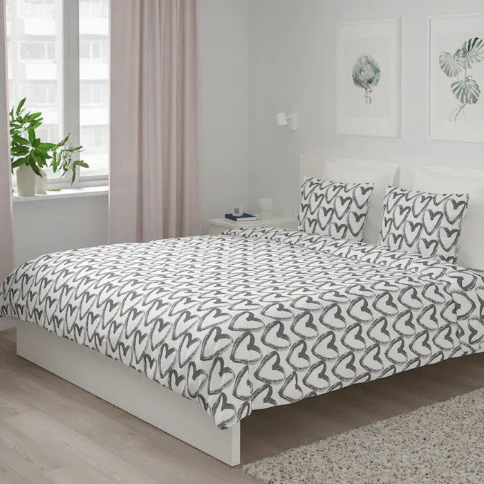 An image of white/grey duvet cover with a love symbol pattern and matching pillowcases arranged on a bed