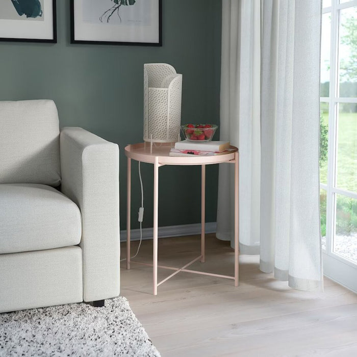 "The IKEA tray table in pale pink shown in a modern living room setting. The table is being used as a side table, showcasing its versatility and trendy design."