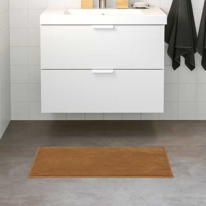 Brown-yellow  bath mat placed on a bathroom floor, featuring a soft and absorbent texture and a non-slip bottom for secure footing 80507986