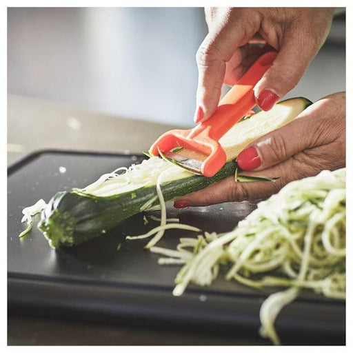 Person peeling courgette into strips using bright orange IKEA UPPFYLLD vegetable cutter on black cutting board