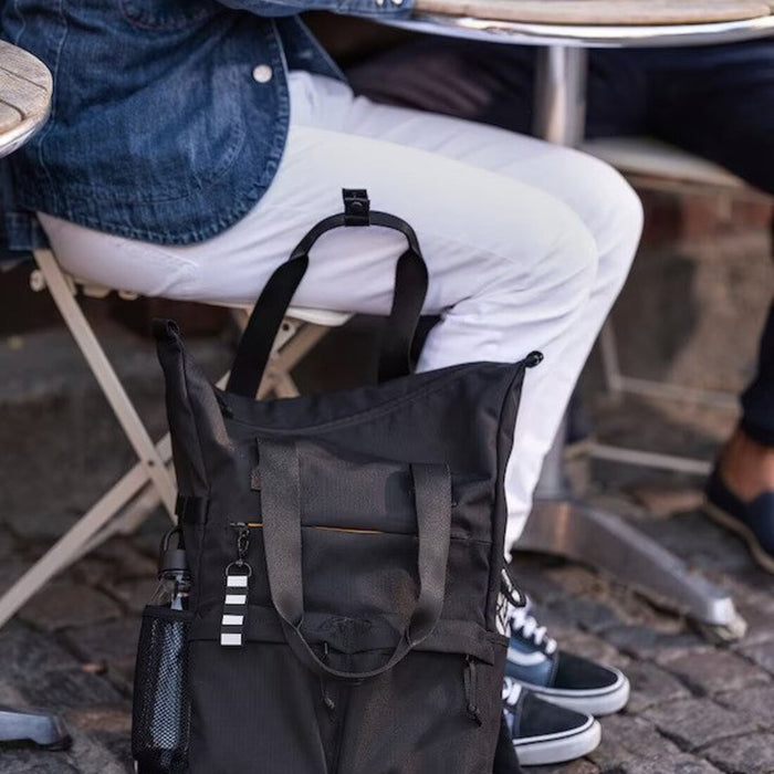 A black and grey IKEA backpack on a wooden table, with a laptop and books inside.