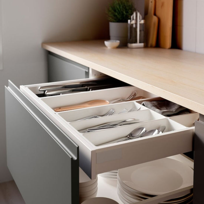 A white plastic cutlery tray designed to fit standard kitchen drawers, with various compartments for storing forks, knives, spoons, and other utensils.