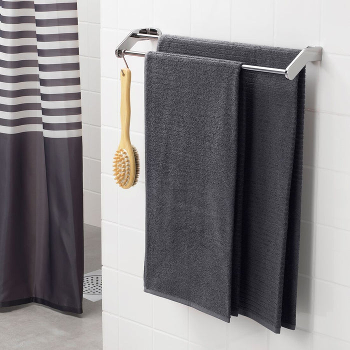 A rolled-up bath towel on a wooden stool next to a bathtub