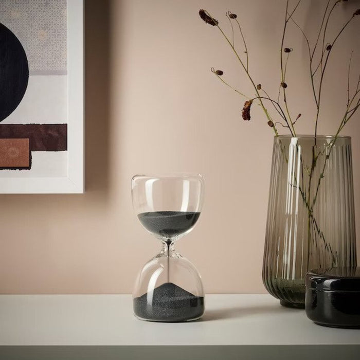A modern hourglass with clear glass and white sand, sitting on a minimalist table.