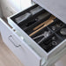 "The IKEA Adjustable Organizer in Grey installed in a kitchen drawer, holding a variety of cooking utensils in its customized compartments."
