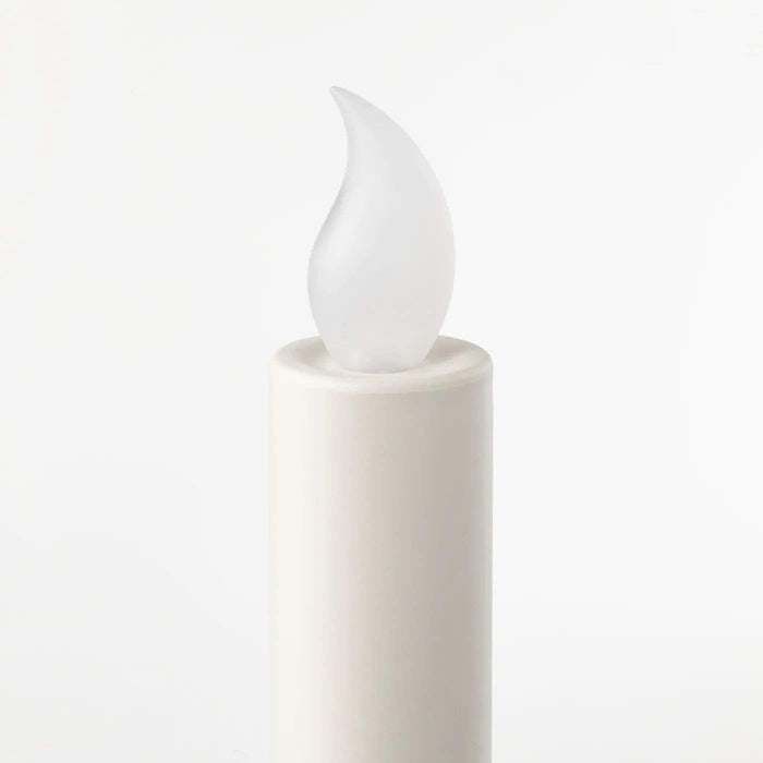 A single white LED candle, battery-operated, with a realistic flame-like light, standing on a black candle holder on a white surface.