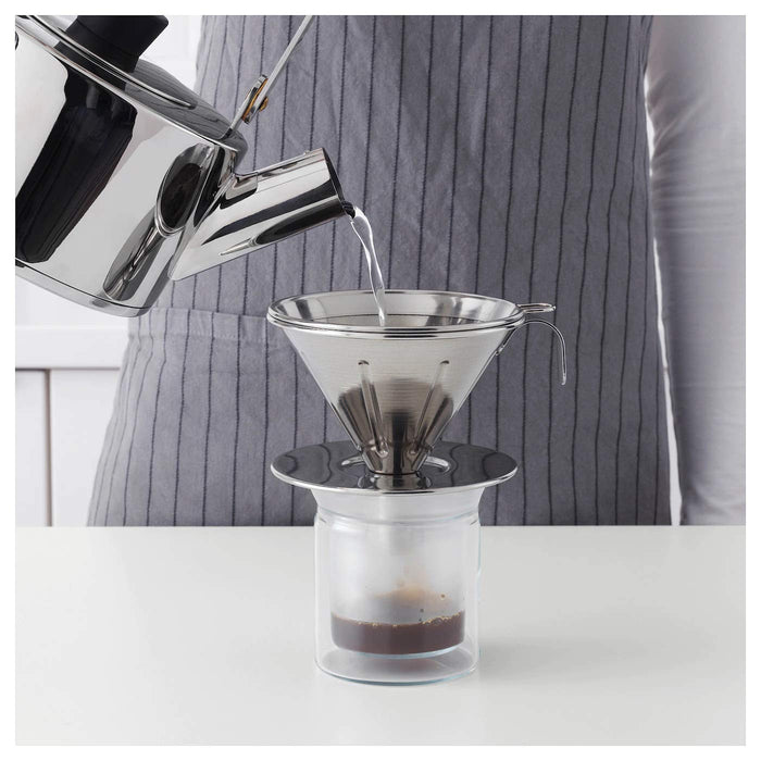 A hand pouring hot water from the metal pour-over kettle into the coffee dripper, showing the precision pouring capabilities of the kettle.