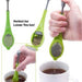  green silicone tea infuser with a handle, suspended in a cup of steaming hot water. 