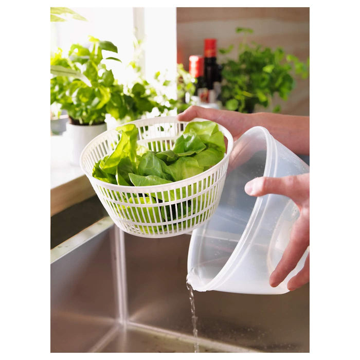 A person's hand holding the clear plastic lid of the IKEA Salad Spinner, with water droplets visible on the surface. 30157235